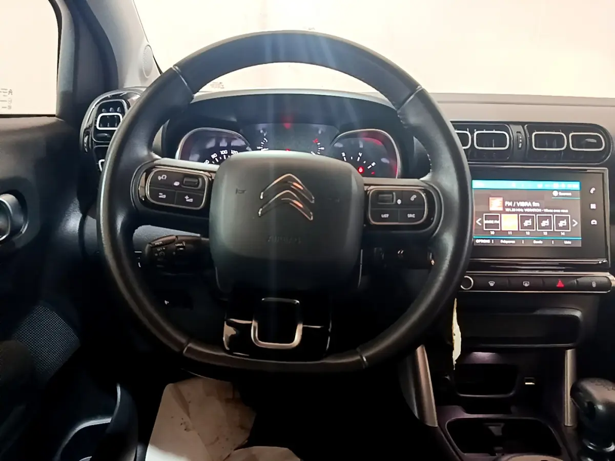 Vue centrée sur le volant cuir noir et le tableau de bord avec écran tactile d'une Citroën C3 Aircross blanche de 2019.