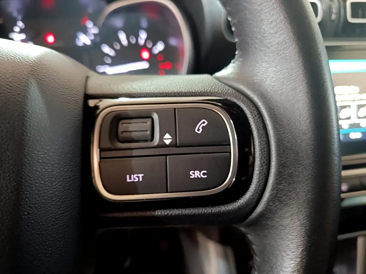 Gros plan sur les commandes gauche du volant cuir noir du Citroën C3 Aircross blanc, tableau de bord flou en arrière-plan.