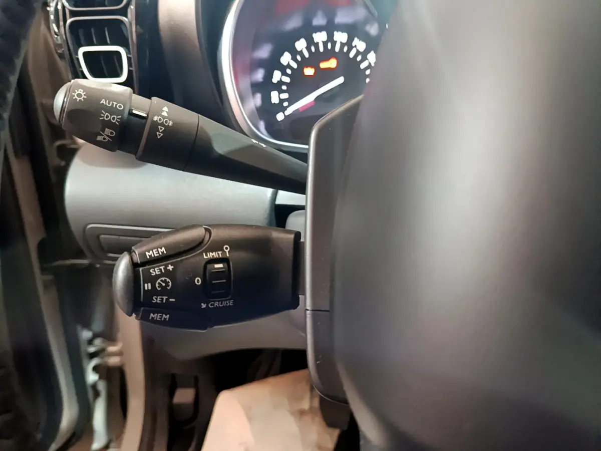 Gros plan sur les commandes de régulateur et feux au volant cuir d'une Citroën C3 Aircross blanche de 2019.