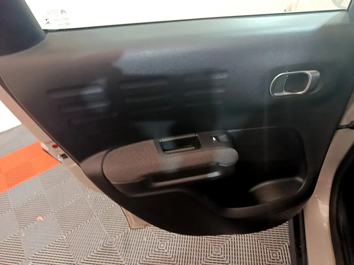 Vue rapprochée de la porte arrière gauche noire intérieure du Citroën C3 Aircross blanc avec poignée et bouton de vitre électrique.