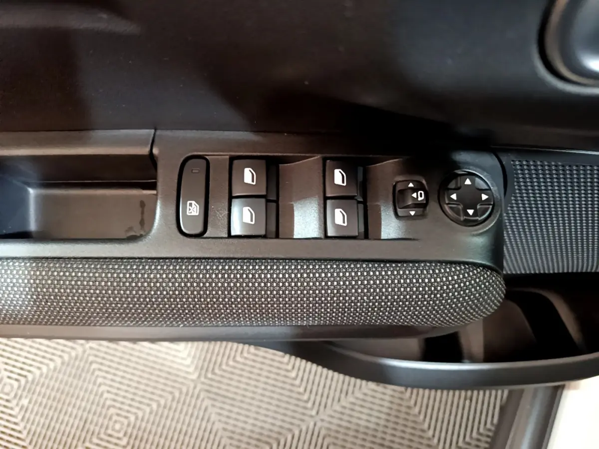 Gros plan sur les commandes de lève-vitres et réglages des rétroviseurs côté conducteur d'une Citroën C3 Aircross blanche.