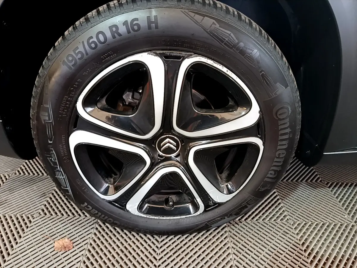 Gros plan sur la roue arrière droite d'une Citroën C3 Aircross blanche, pneu Continental visible sur sol texturé.