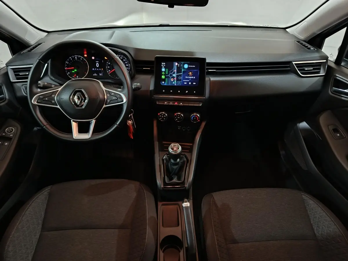 Vue intérieure avant de la Renault Clio gris clair 2023, tableau de bord avec écran tactile et volant multifonctions cuir.
