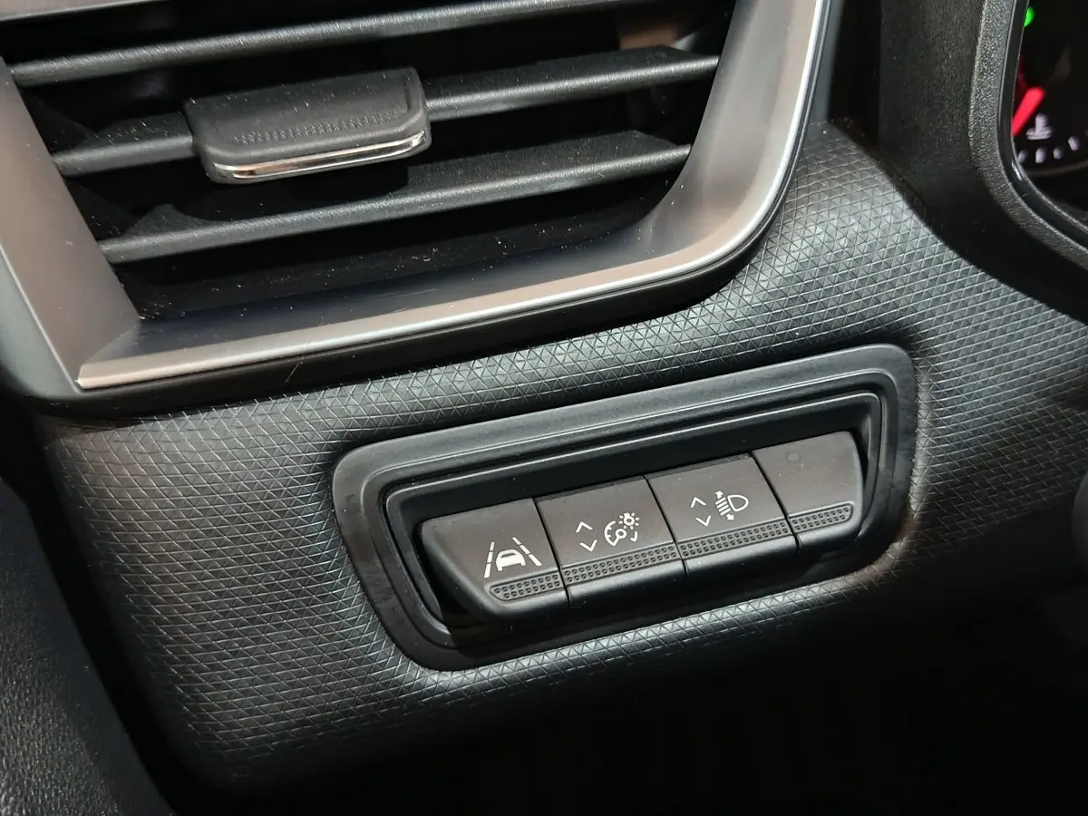 Gros plan sur les commandes d'assistance à la conduite et réglage des phares dans l'habitacle noir de la Renault Clio gris clair.