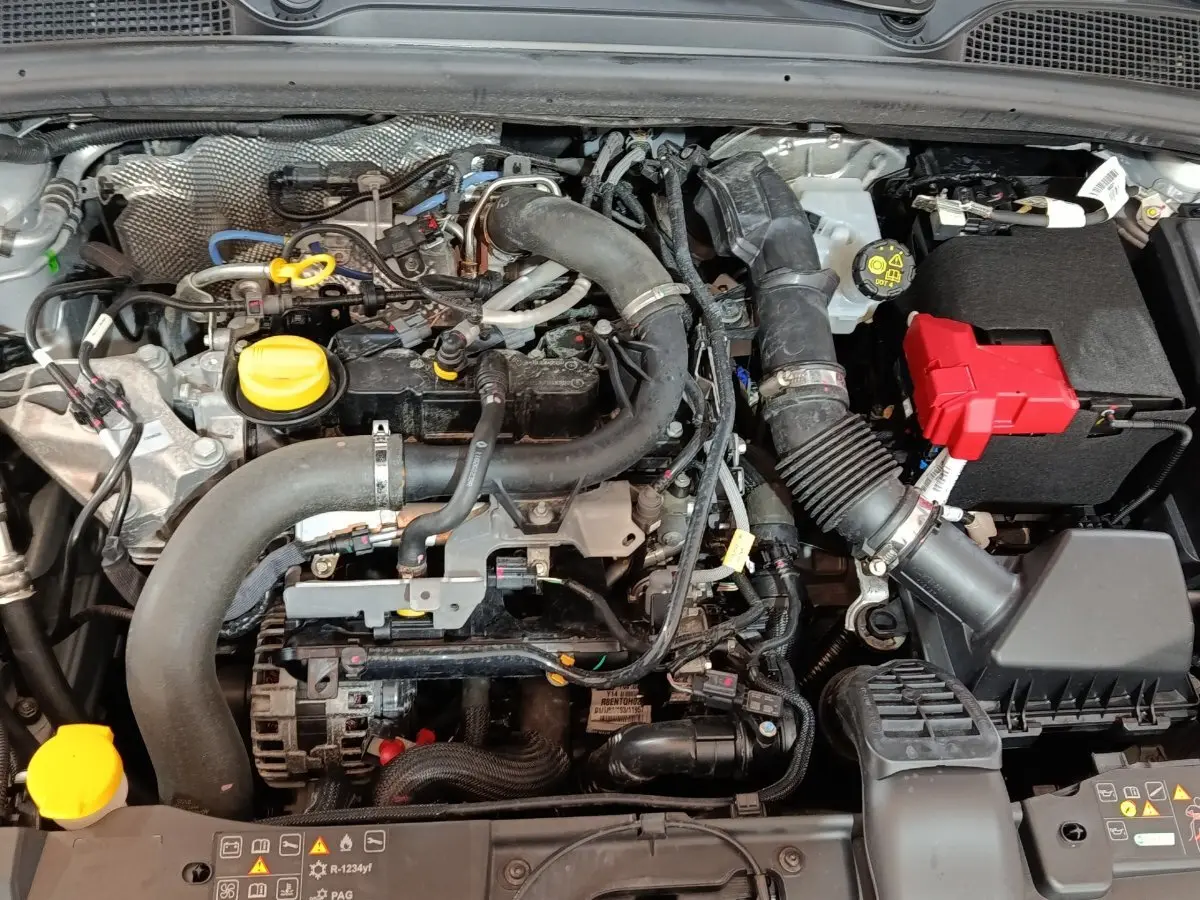 Gros plan sur le moteur essence d'une Renault Clio 2023, avec bouchons jaunes et batterie à capot rouge visible.