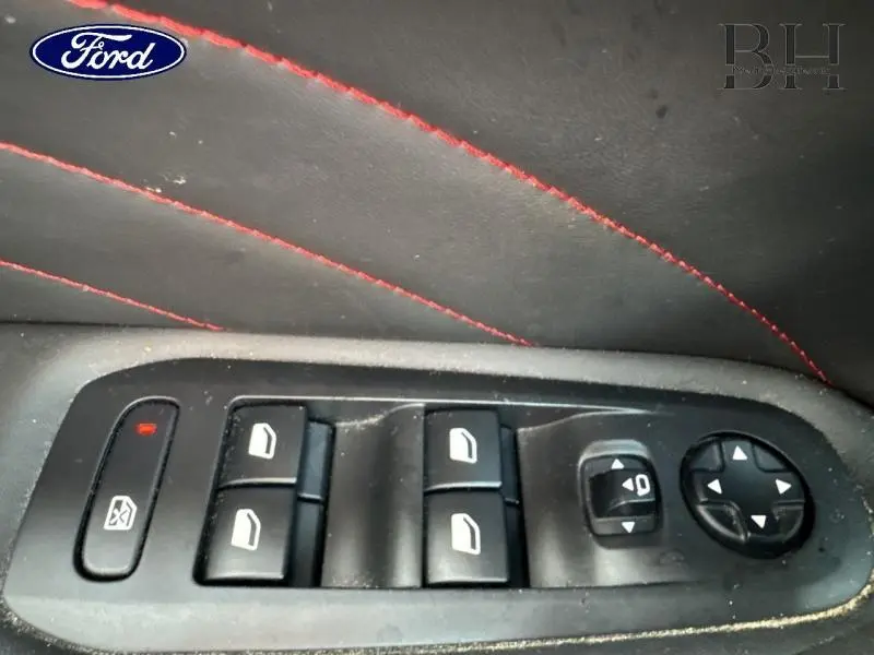 Panneau de commandes des vitres et rétroviseurs côté conducteur avec surpiqûres rouges sur cuir noir.