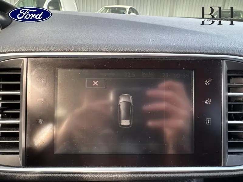 Écran tactile intérieur affichant la vue top-down d’un véhicule gris, avec reflets de mains visibles.