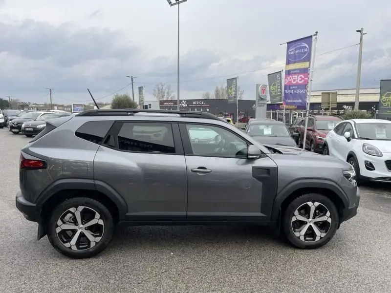 Vue de profil côté droit du Dacia Duster 1.6 Hybrid 140 cv Journey 2025 en gris schiste avec jantes distinctives.