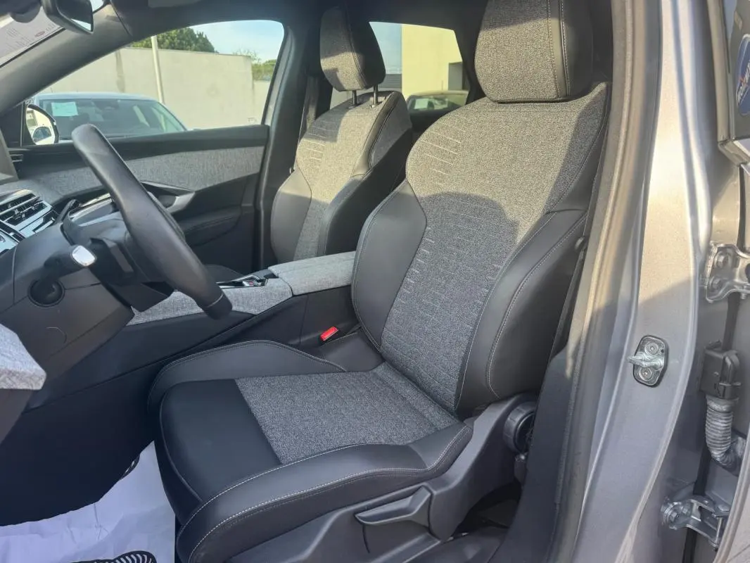 Vue intérieure côté conducteur du Peugeot 3008 Hybrid gris 2025, sièges tissu et cuir bicolore avec console centrale visible.