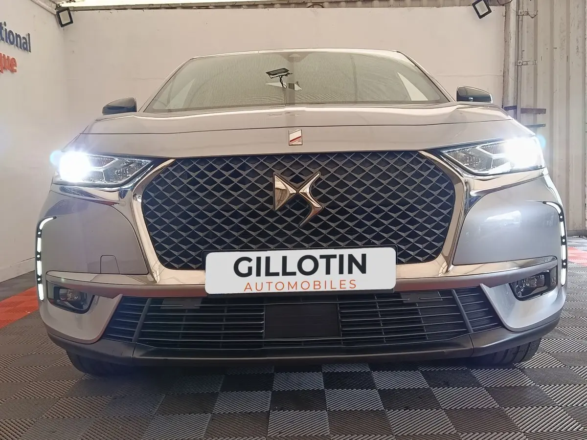 Vue frontale d'un DS7 Crossback E-TENSE gris clair avec phares allumés et calandre distinctive en losanges.