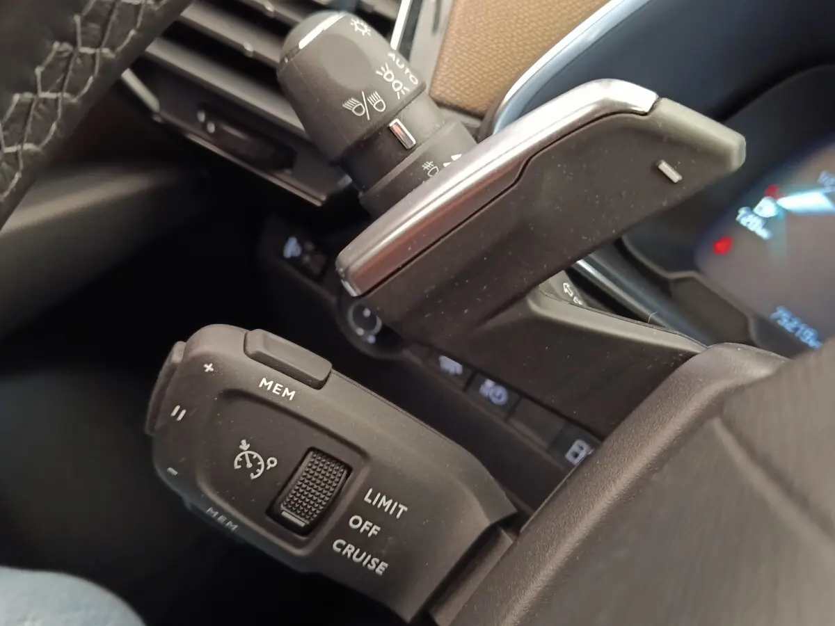 Gros plan sur les commandes au volant cuir noir du DS7 Crossback E-TENSE 225, avec régulateur de vitesse et palettes de boîte auto.