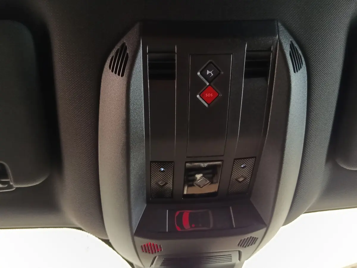 Vue en gros plan du plafonnier noir avec bouton SOS rouge et commandes d’éclairage du DS7 Crossback gris clair.