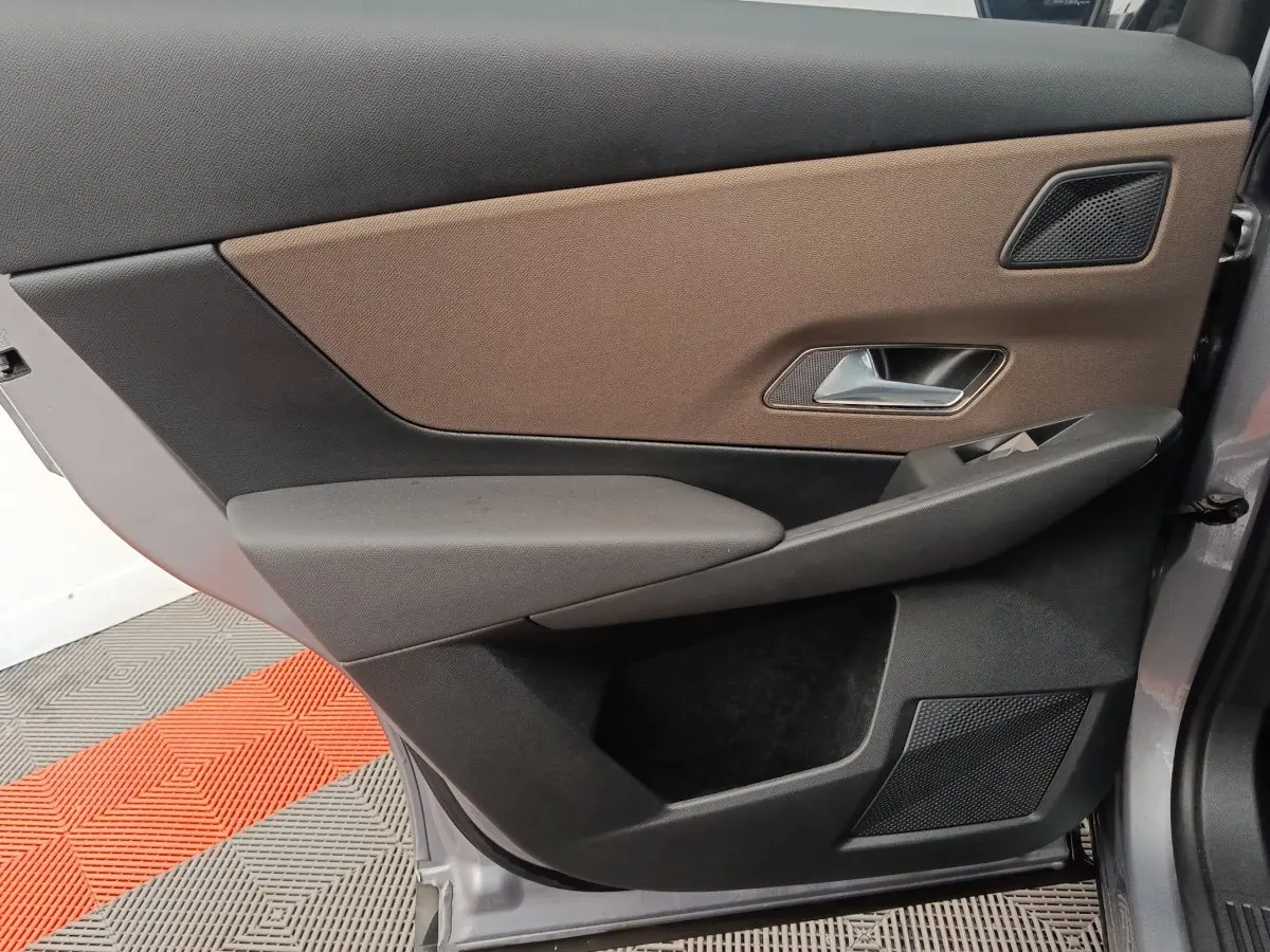 Vue rapprochée de la porte avant droite du DS7 Crossback gris clair, avec habillage marron et noir et poignée argentée.