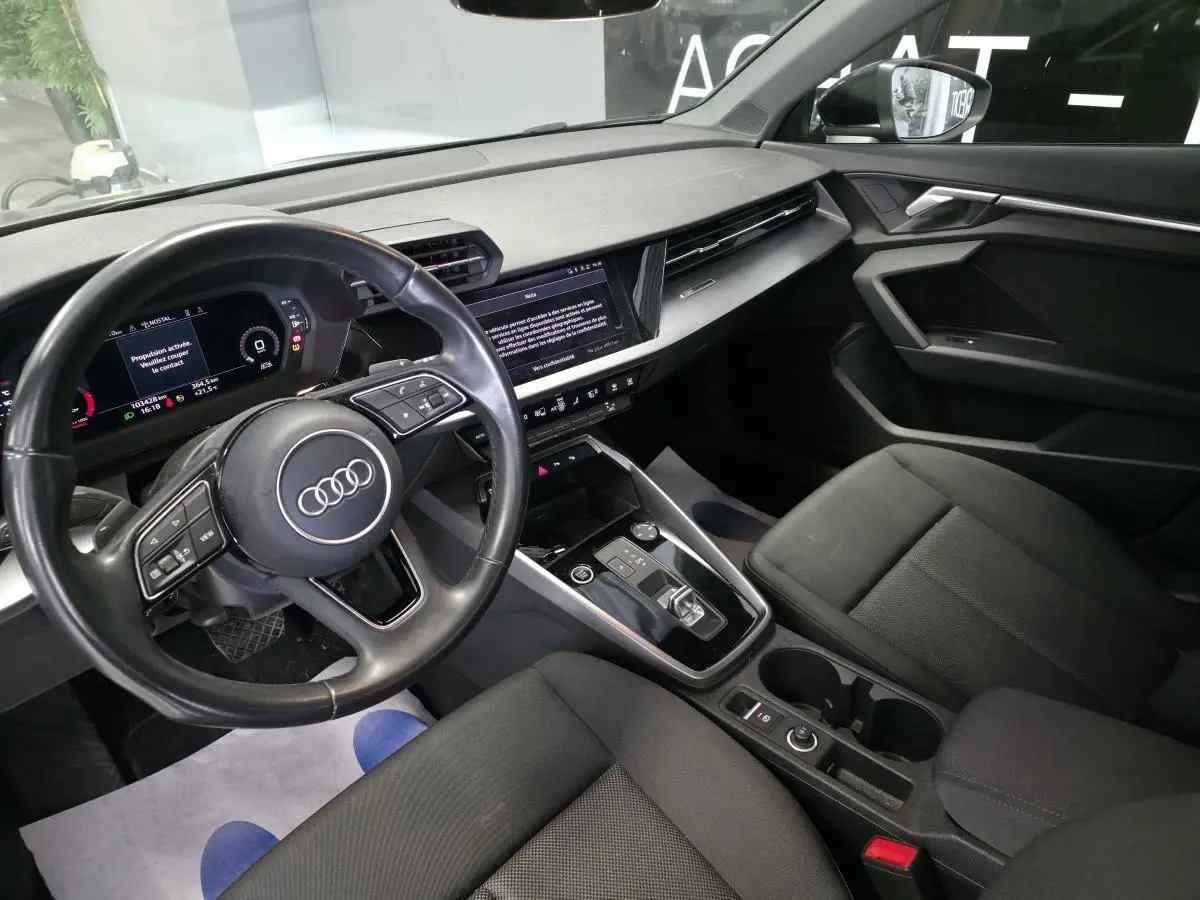 Vue intérieure côté conducteur de l'Audi A3 Sportback 2023 avec tableau de bord digital et sellerie tissu noire.