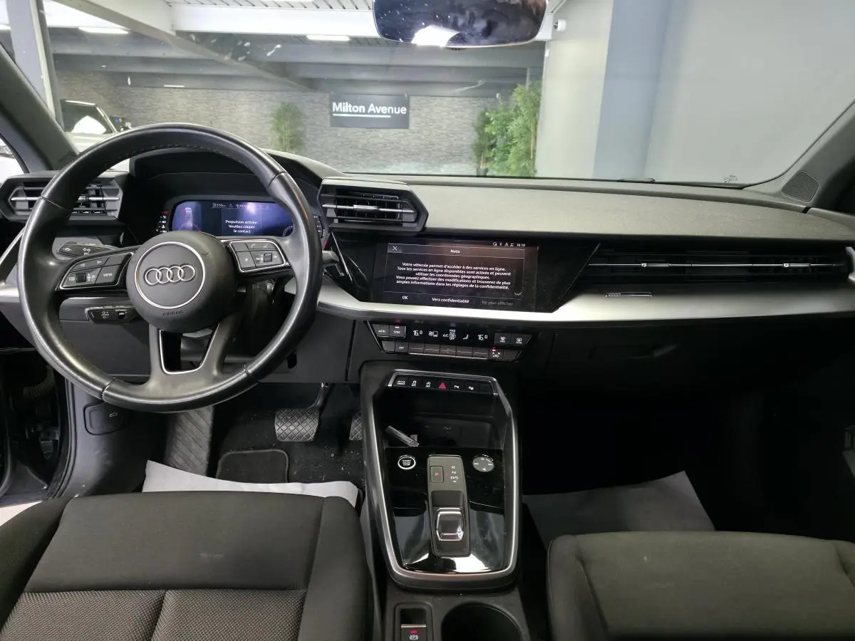 Vue intérieure avant de l'Audi A3 Sportback 2023, tableau de bord noir avec écran digital et volant cuir multifonctions.