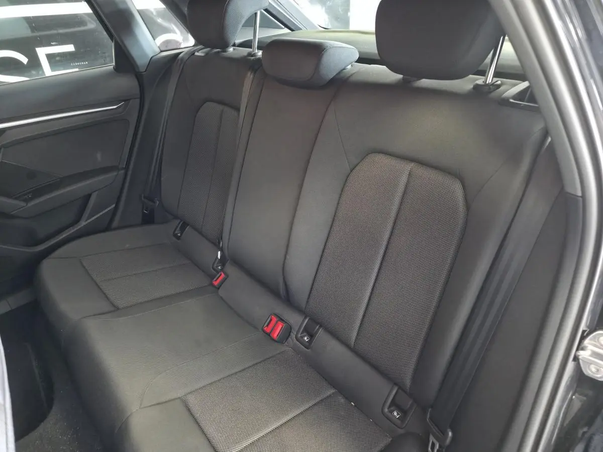 Vue intérieure côté arrière droit de la banquette tissu noire de l'Audi A3 Sportback 2023 avec appuie-têtes et ceintures visibles.