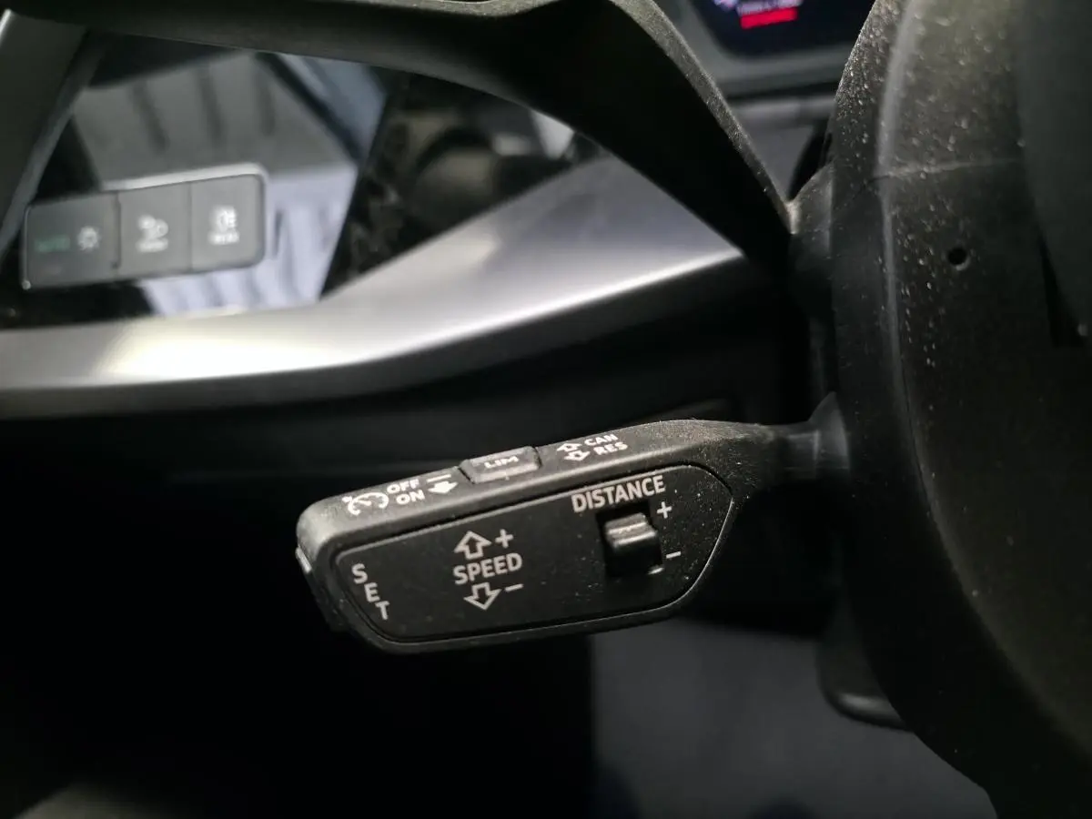 Gros plan sur la commande de régulateur de vitesse adaptatif à gauche du volant d’un Audi A3 Sportback noir 2023.