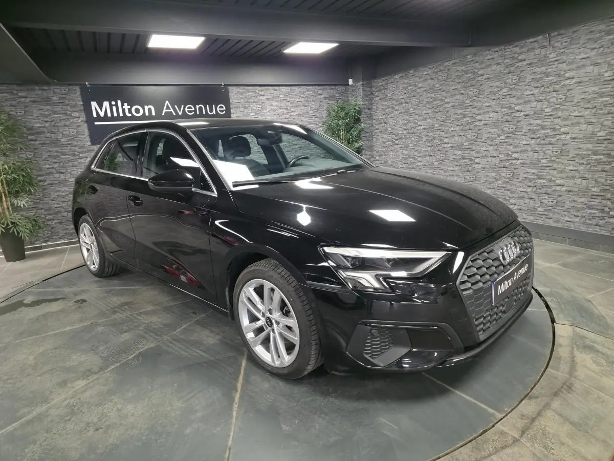 Audi A3 Sportback noir vue 3/4 avant droit en intérieur avec calandre noire et jantes alliage 17 pouces.