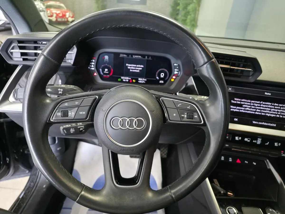Vue intérieure centrée sur le volant cuir noir multifonctions de l'Audi A3 Sportback 2023 avec tableau de bord digital.