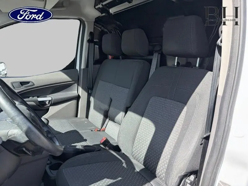 Vue intérieure côté conducteur du Ford Transit Connect blanc glacier, montrant la banquette passagers et le volant multifonction.