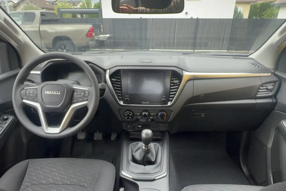Vue intérieure avant de l'Isuzu D-MAX 2026 avec tableau de bord noir, volant multifonctions et écran tactile central.