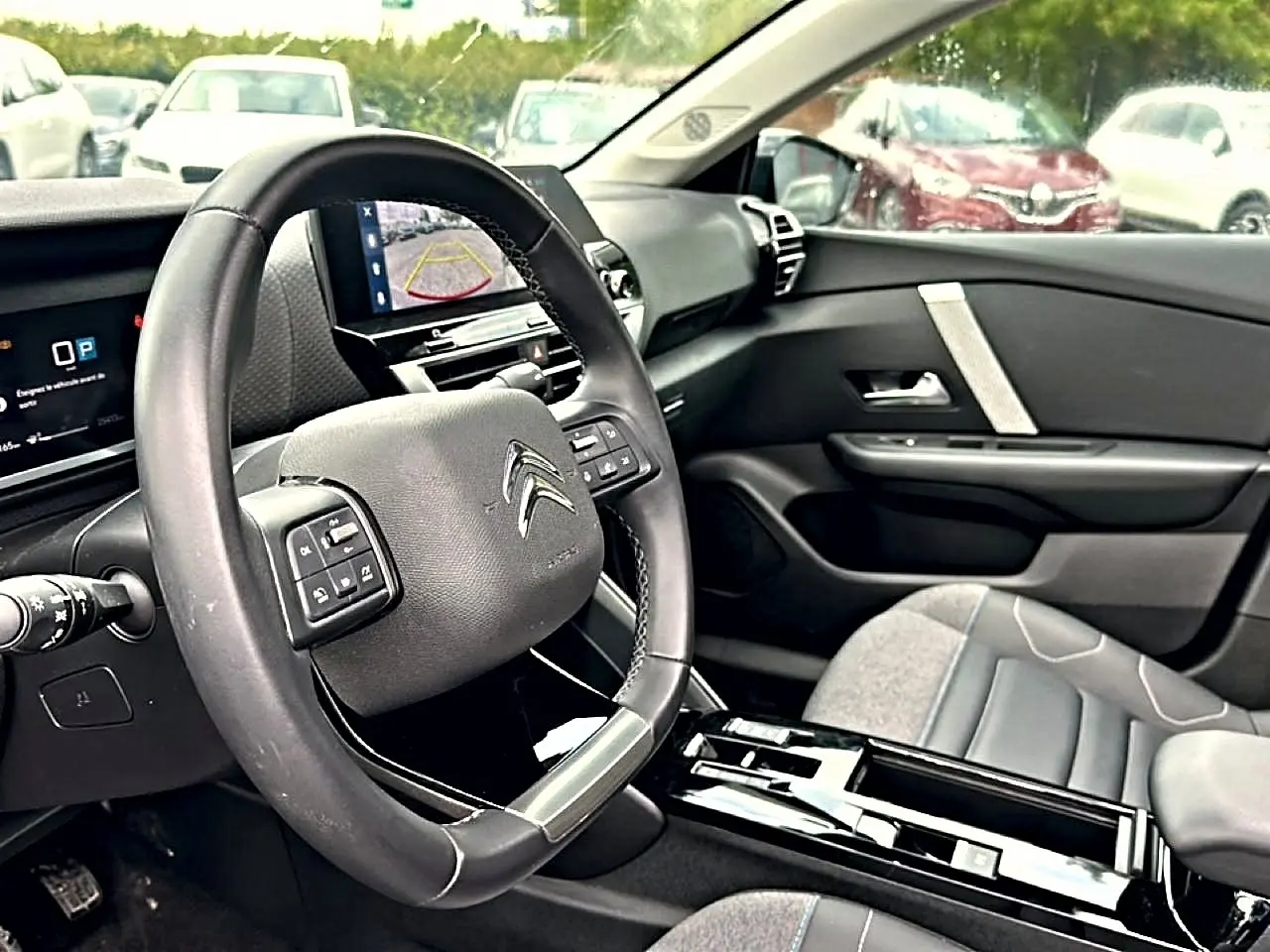 Vue intérieure côté conducteur de la Citroën C4 2024, volant cuir noir et écran tactile affichant la caméra de recul.