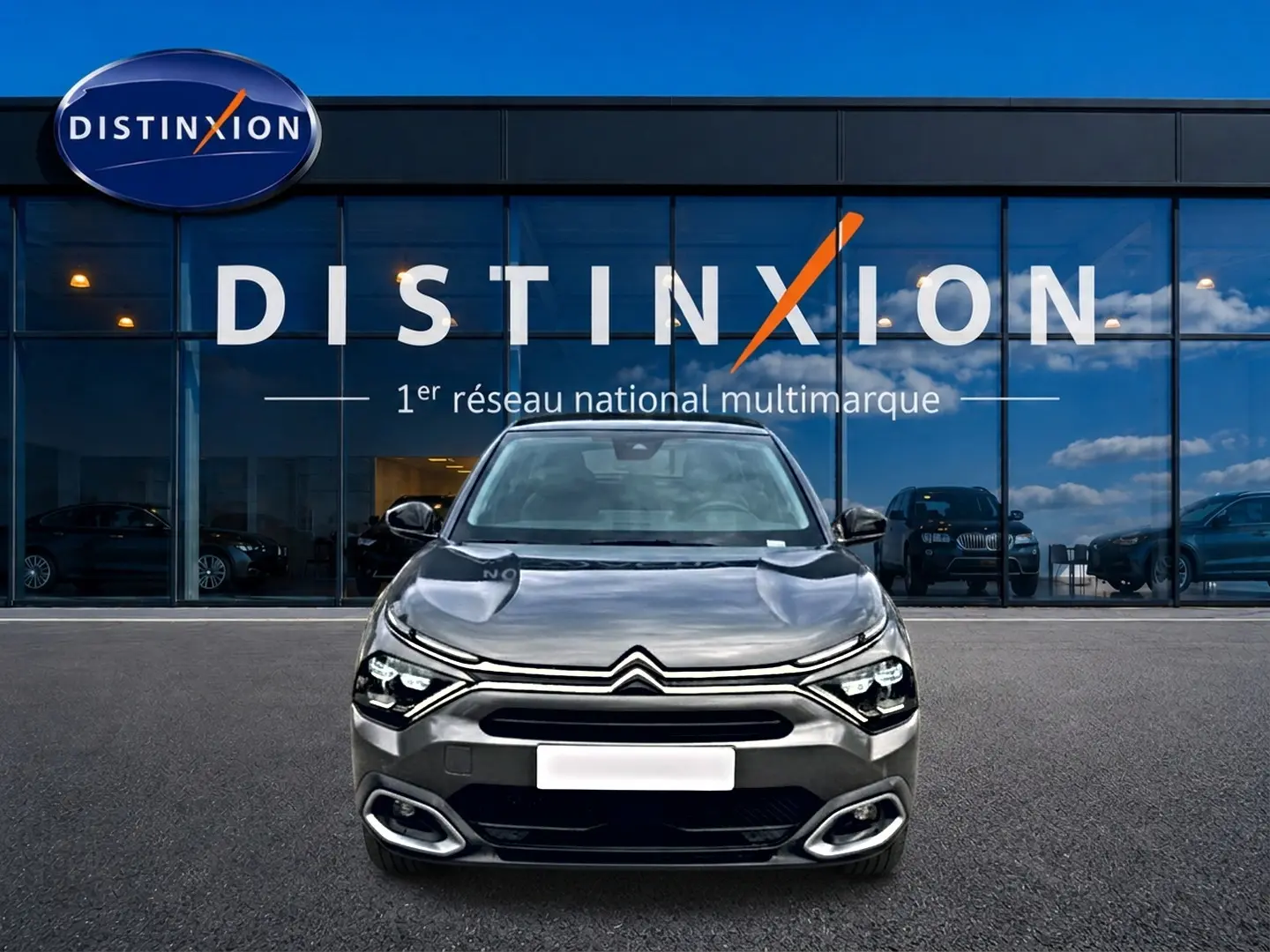 Citroën C4 gris 2024 vue de face, avec phares LED et calandre distinctive devant un showroom Distinxion.