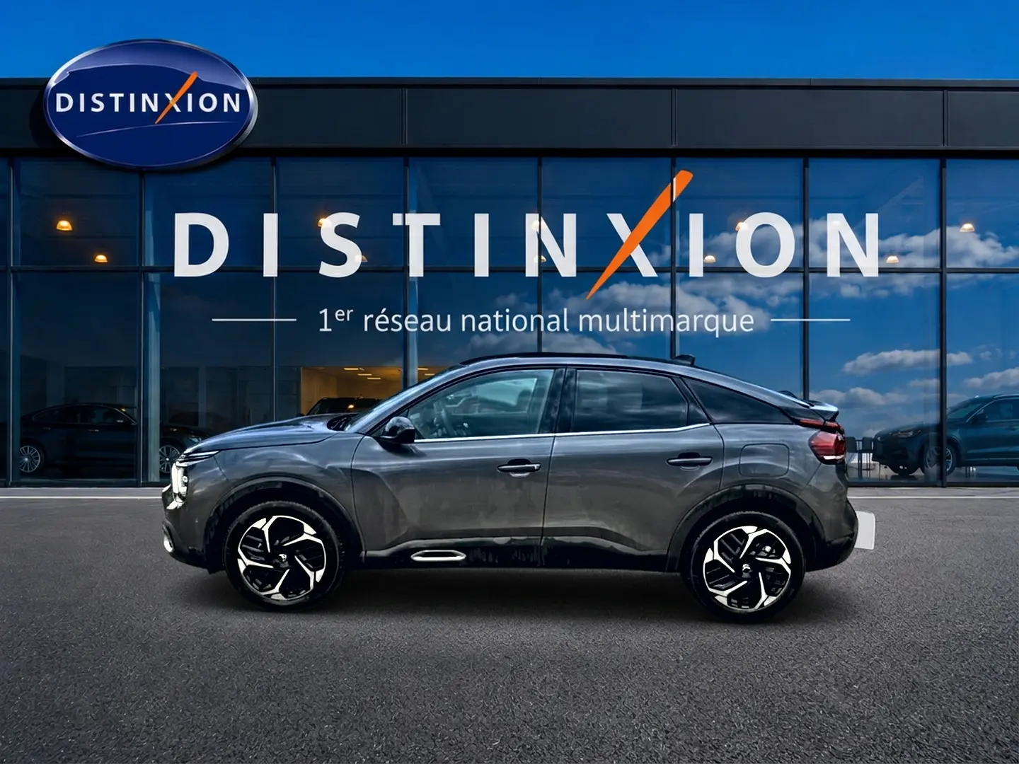 Profil côté gauche d'une Citroën C4 gris 2024 avec jantes alu noires et toit noir devant un bâtiment Distinxion.