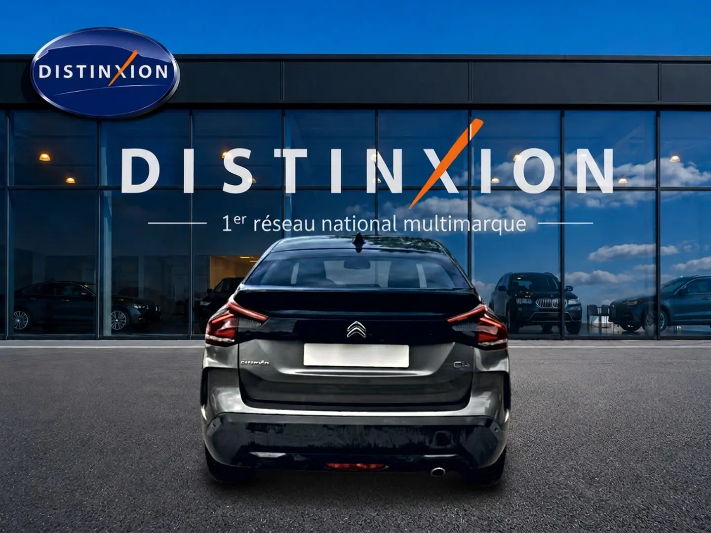 Vue arrière d'une Citroën C4 gris métallisé 2024, stationnée devant une vitrine avec logo Distinxion.