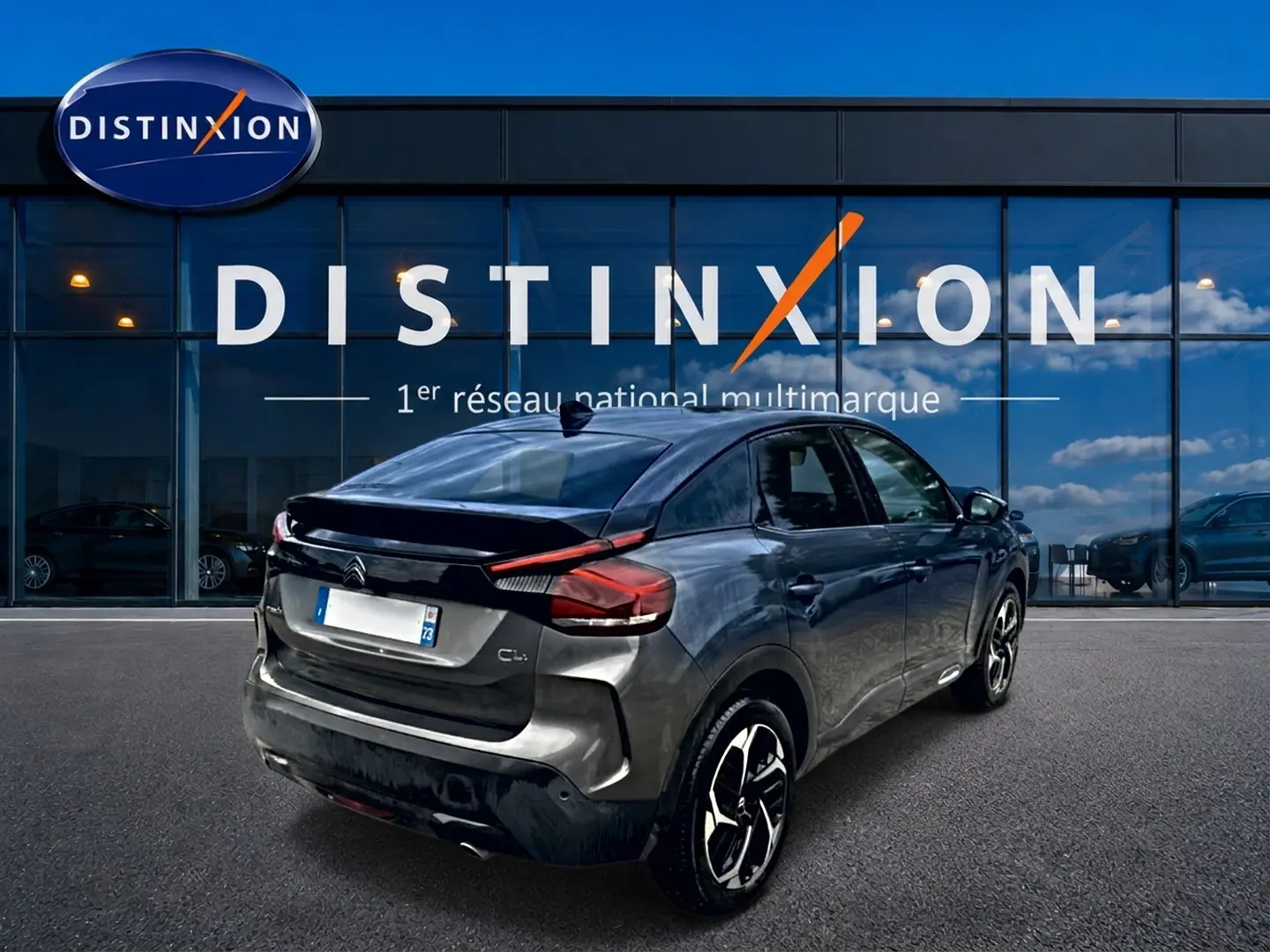 Vue 3/4 arrière droite d'une Citroën C4 gris métallisé avec jantes alu, devant une vitrine Distinxion.