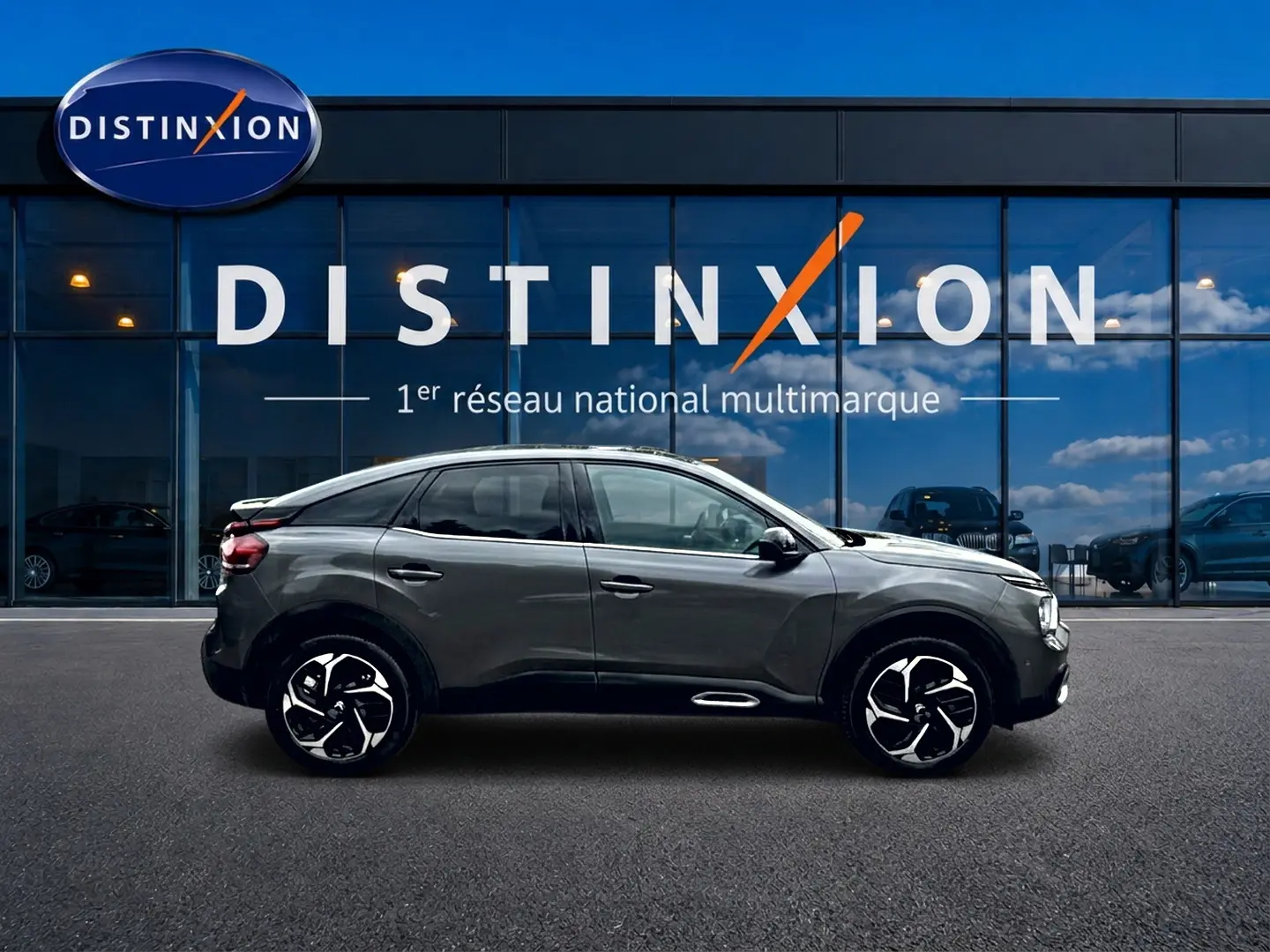 Profil droit d'une Citroën C4 gris 2024 avec jantes alu noires et vitres arrière surteintées, devant une vitrine Distinxion.