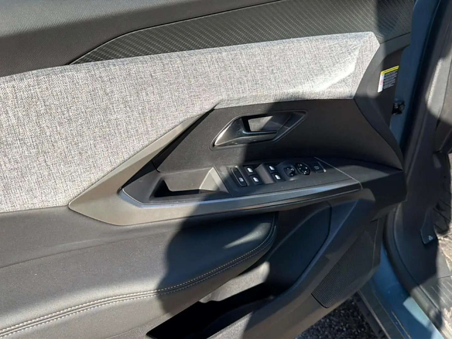 Détail de la porte avant gauche du Peugeot 3008 bleu 2025, montrant les commandes des vitres et le revêtement tissu et cuir.