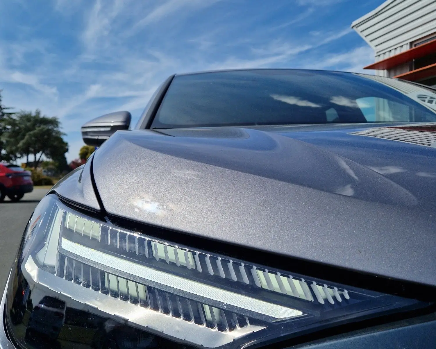 Gros plan sur le phare avant gauche de l'Audi Q4 E-TRON SPORTBACK gris thyphon sous un ciel bleu lumineux.