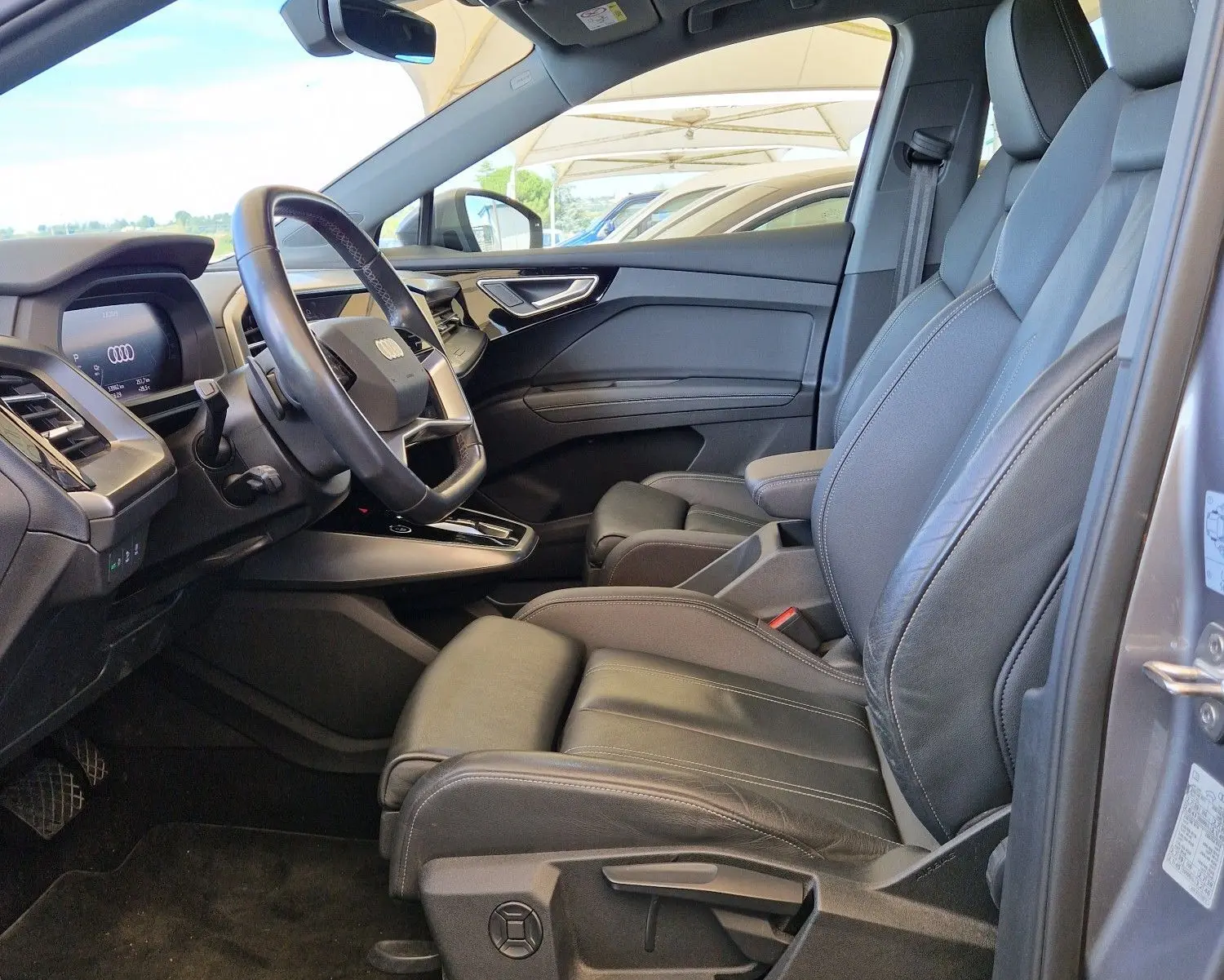 Vue intérieure côté conducteur de l'Audi Q4 E-TRON Sportback gris thyphon, sièges cuir noir et toit panoramique.