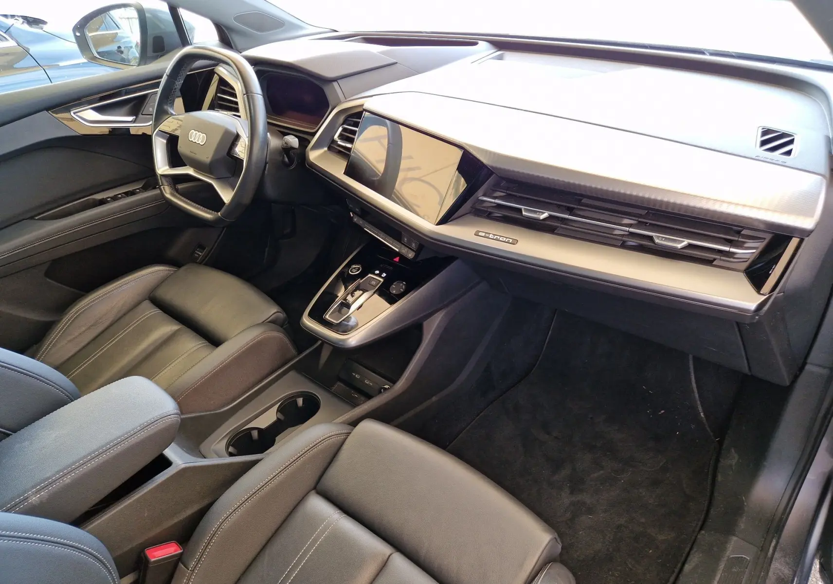 Intérieur noir de l'Audi Q4 E-TRON SPORTBACK 50 quattro, vue côté conducteur mettant en valeur le tableau de bord moderne.