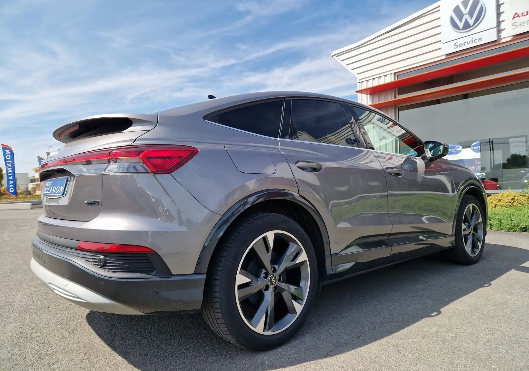 Audi Q4 E-TRON Sportback gris thyphon vu en 3/4 arrière droit, soulignant ses lignes fluides et ses jantes modernes.