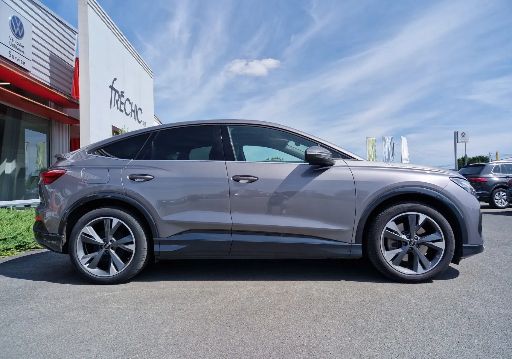 Audi Q4 E-TRON Sportback gris thyphon vu de profil côté gauche, soulignant ses grandes jantes et silhouette électrique élégante.