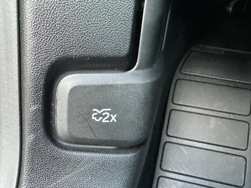 Gros plan sur le bouton de déverrouillage du coffre avec symbole 2x dans l'habitacle d'une Ford Focus noire.