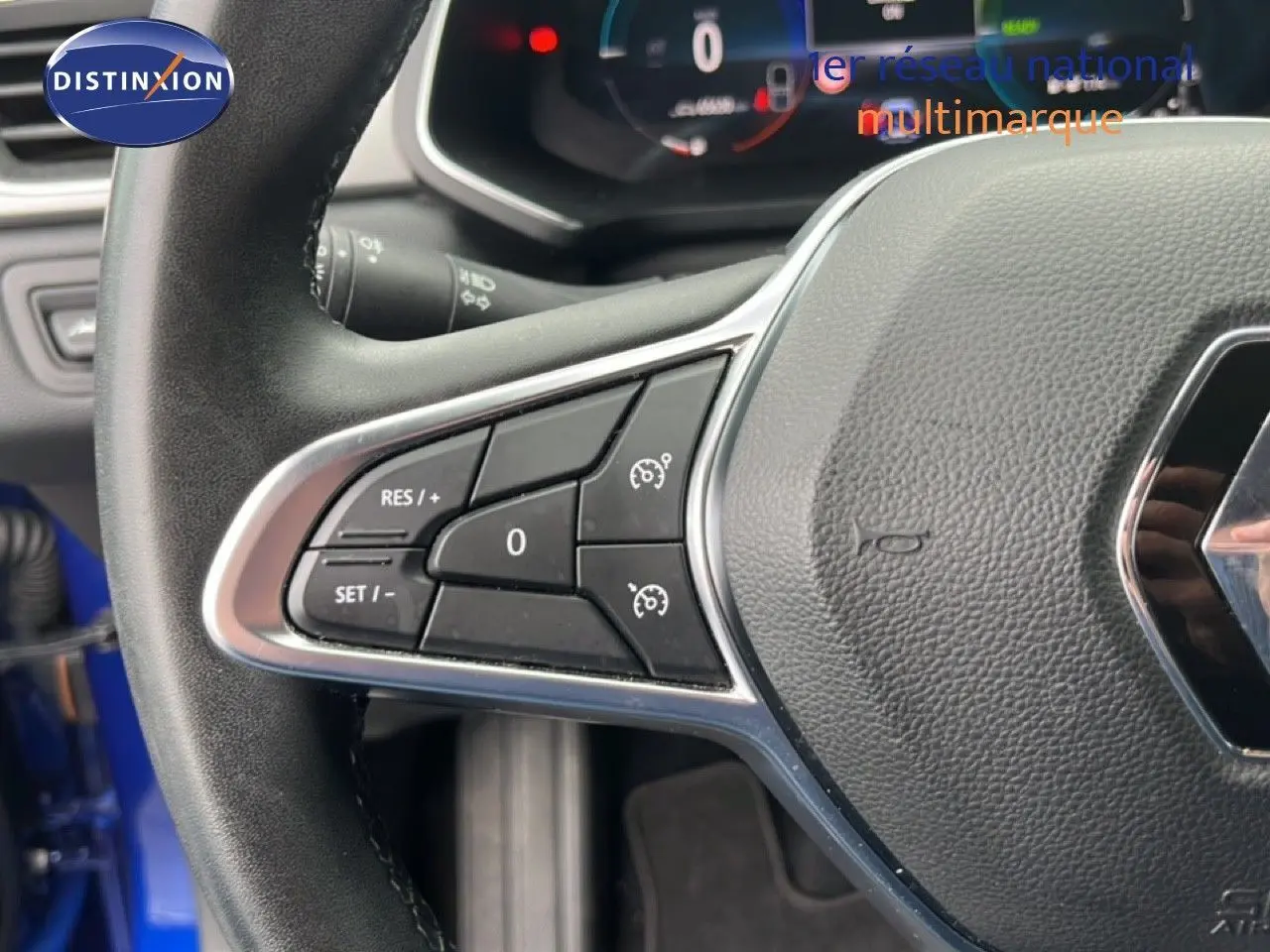 Gros plan sur le volant noir du Renault Captur bleu Iron Metal, avec commandes intégrées et logo Renault visible.