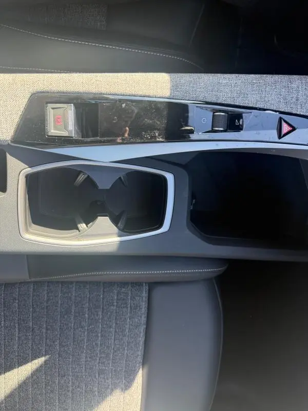 Vue plongeante sur la console centrale grise du Peugeot 3008 Hybrid 145, avec porte-gobelets et commandes de frein à main électrique.