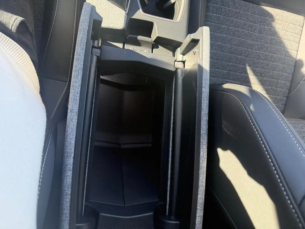 Vue plongeante sur la console centrale ouverte du Peugeot 3008 Hybrid gris, montrant le rangement intérieur et les sièges tissu.