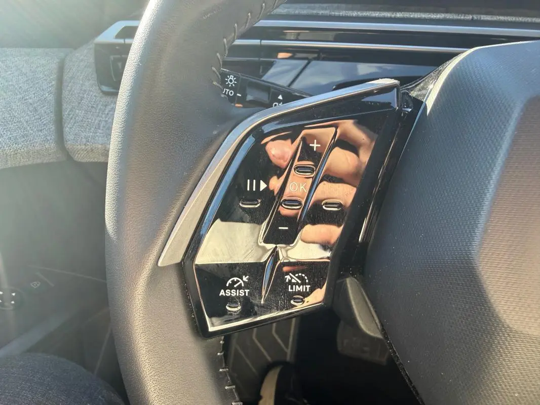 Gros plan sur les commandes gauche du volant du Peugeot 3008 Hybrid gris, avec boutons de régulateur et limiteur de vitesse.