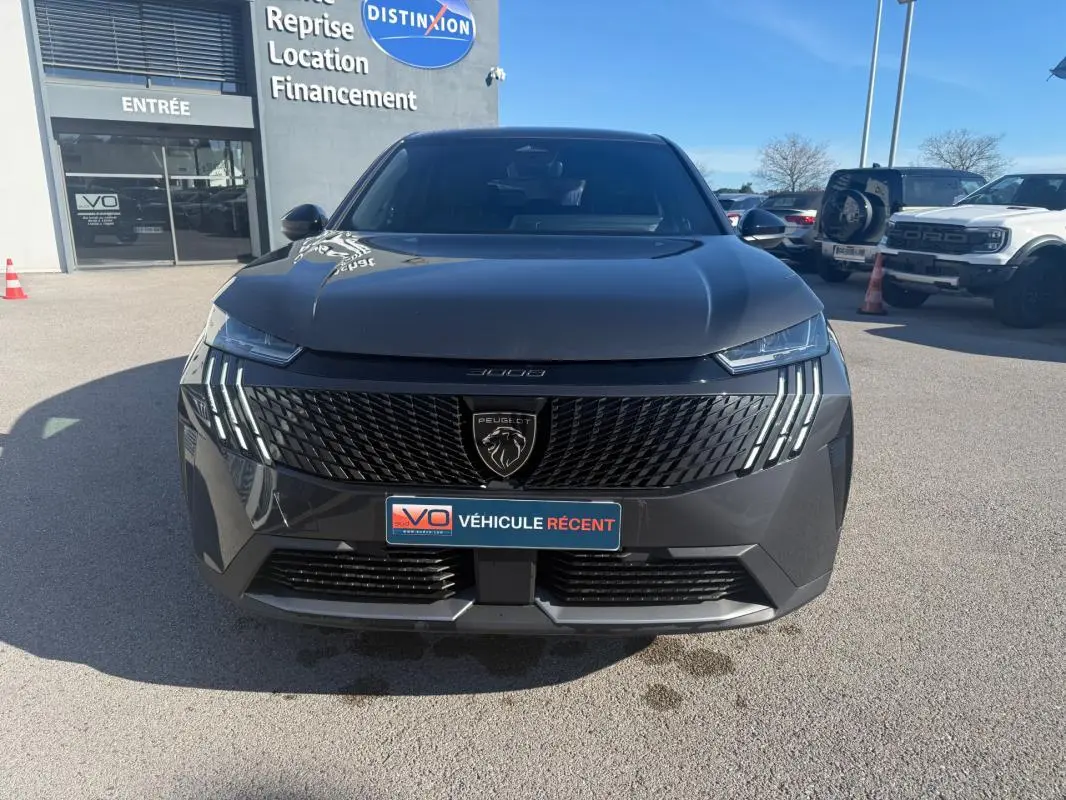 Vue frontale d'un Peugeot 3008 Hybrid gris avec calandre noire et feux LED distinctifs, stationné en extérieur.