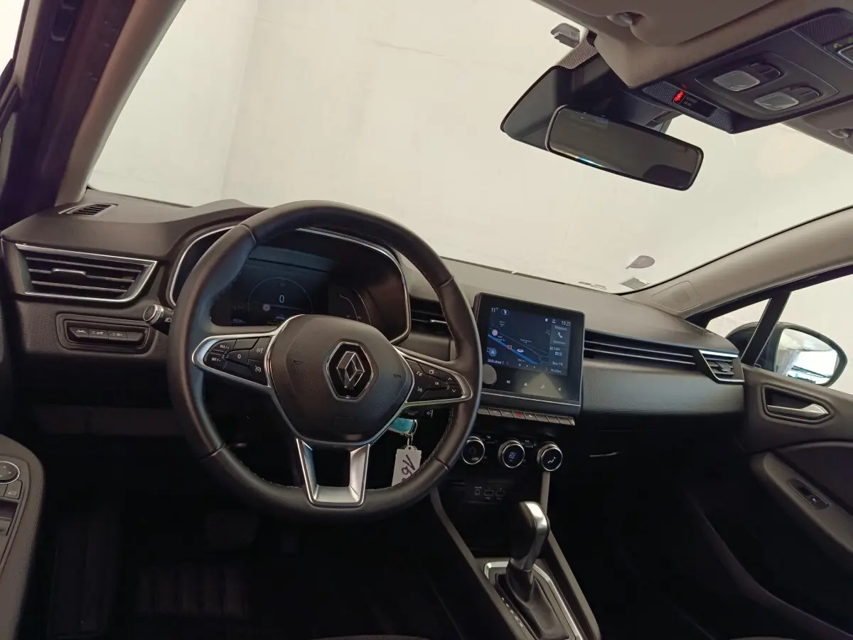 Vue intérieure côté conducteur de la Renault Clio Business E-TECH 140 avec volant cuir et écran tactile central allumé.