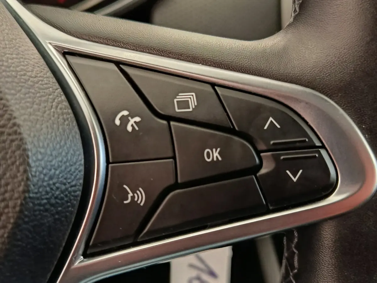 Gros plan sur les commandes multifonctions noires du volant côté gauche de la Renault Clio Business E-TECH blanche.