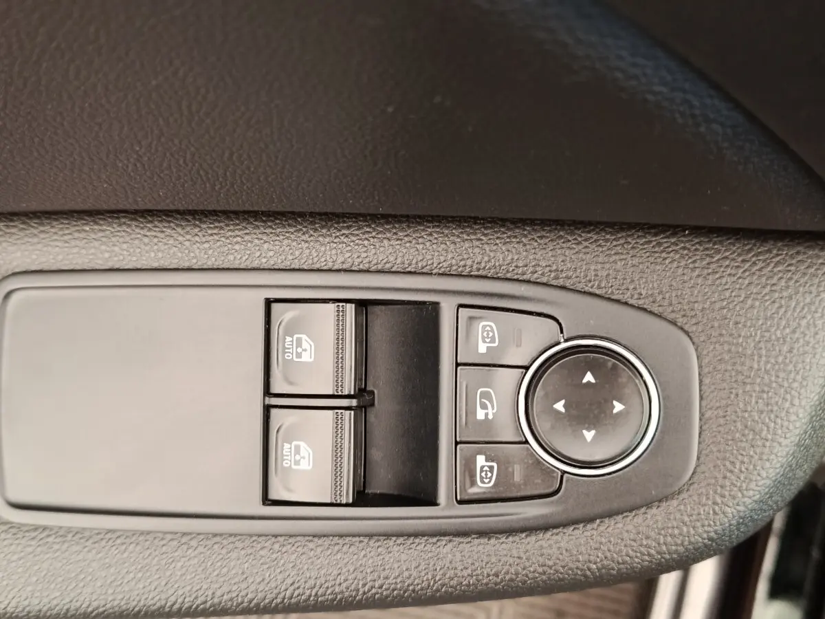 Gros plan sur les commandes de lève-vitres et réglage des rétroviseurs côté conducteur d'une Renault Clio Business E-TECH blanche.