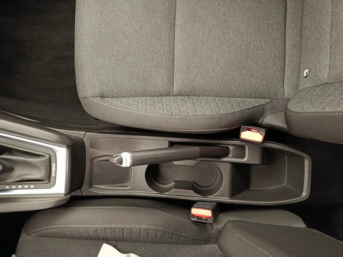 Vue plongeante sur la console centrale noire de la Renault Clio Business E-TECH 140 avec frein à main manuel et sièges tissu gris.