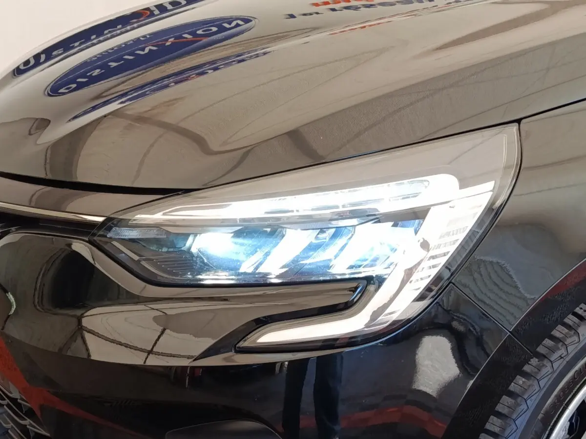 Gros plan sur le phare avant droit allumé d’une Renault Clio noire, soulignant son design LED moderne.