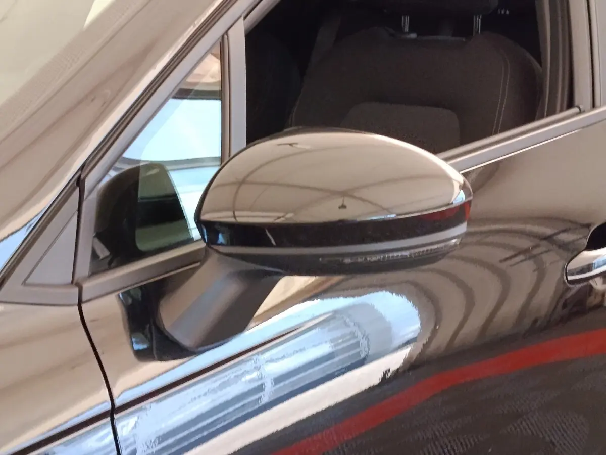 Gros plan sur le rétroviseur droit noir brillant d'une Renault Clio Business E-TECH 140, avec reflet sur la carrosserie noire.