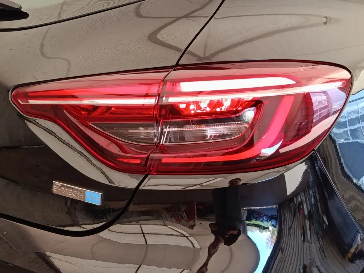 Gros plan sur le feu arrière droit rouge d’une Renault Clio Business E-TECH 140 noire avec badge hybride bleu.